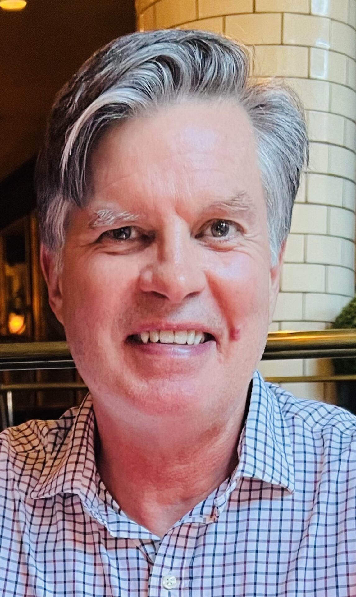 A man with gray hair and wearing a checkered shirt.